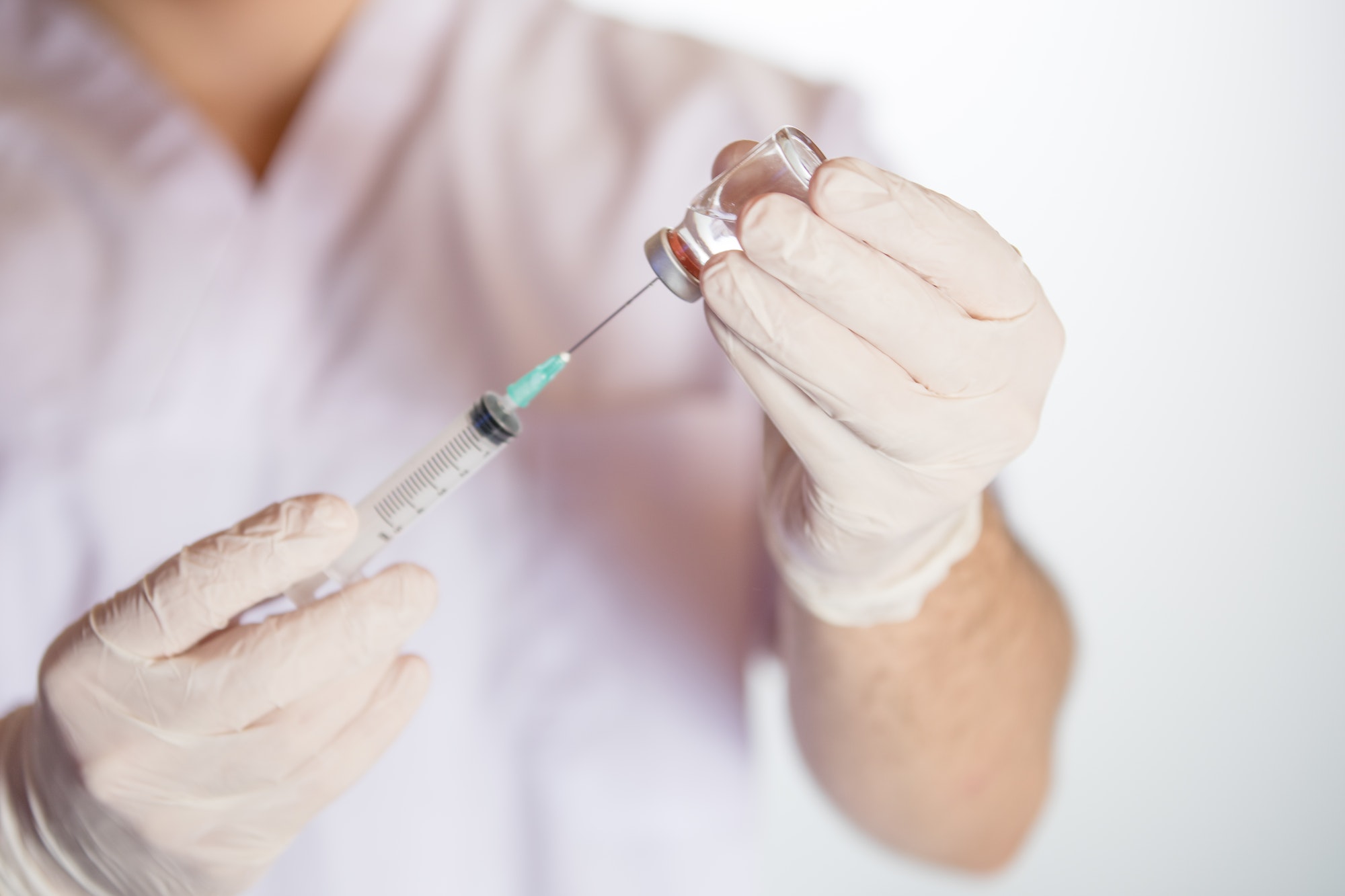 Health worker drawing vaccine in vial into syringe for COVID-19, measles, flu shots