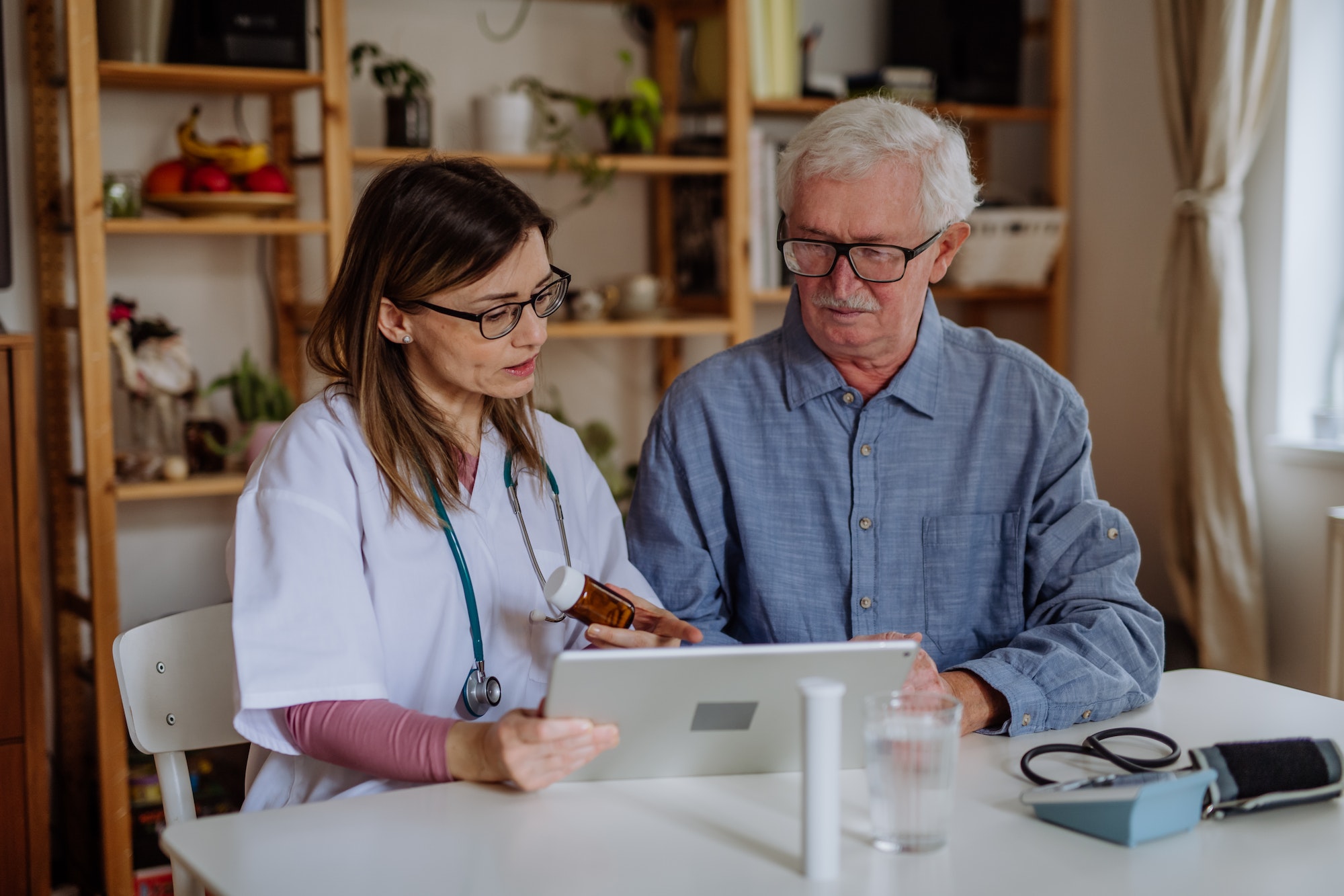 Healthcare worker or caregiver visiting senior man indoors at home, explaining medicine dosage.